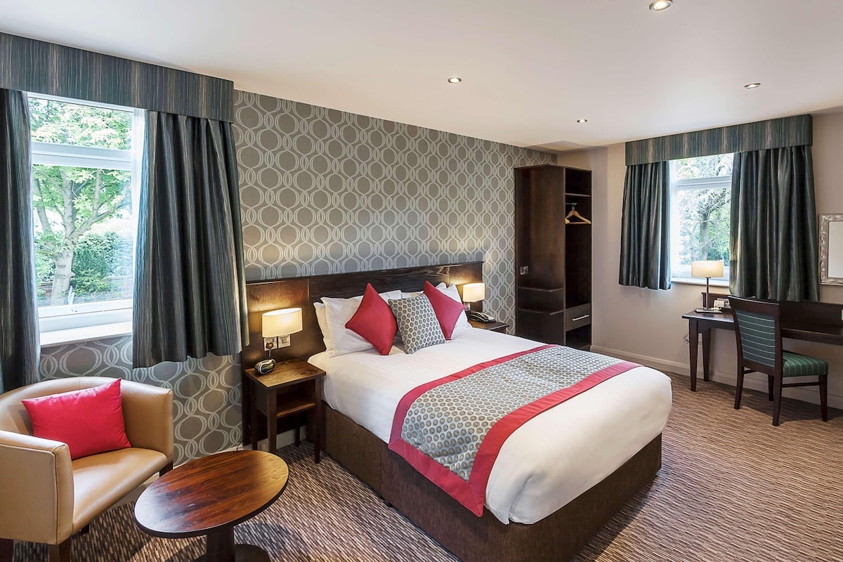 A hotel room with a large bed, a desk, a chair, and a small table.