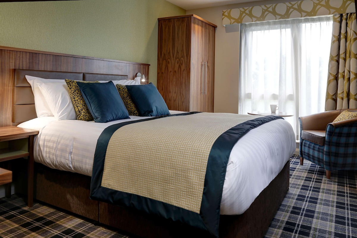 Een hotelkamer met een groot bed, een kledingkast, een stoel en een raam met gordijnen.