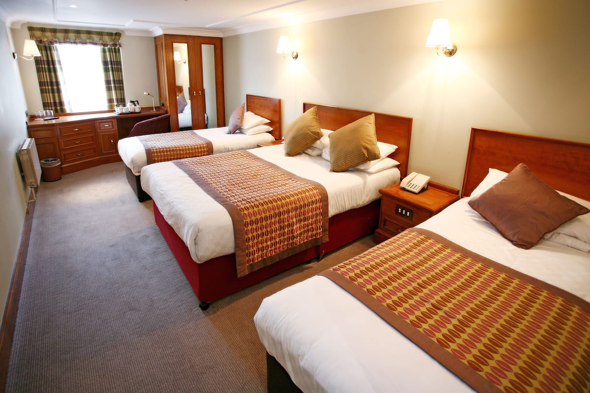 Ein Hotelzimmer mit drei Betten, einem Schreibtisch und einem Spiegel.