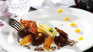 Une assiette blanche contenant un dessert composé de sphères de chocolat, d’une part de gâteau rectangulaire et de quelques décorations.