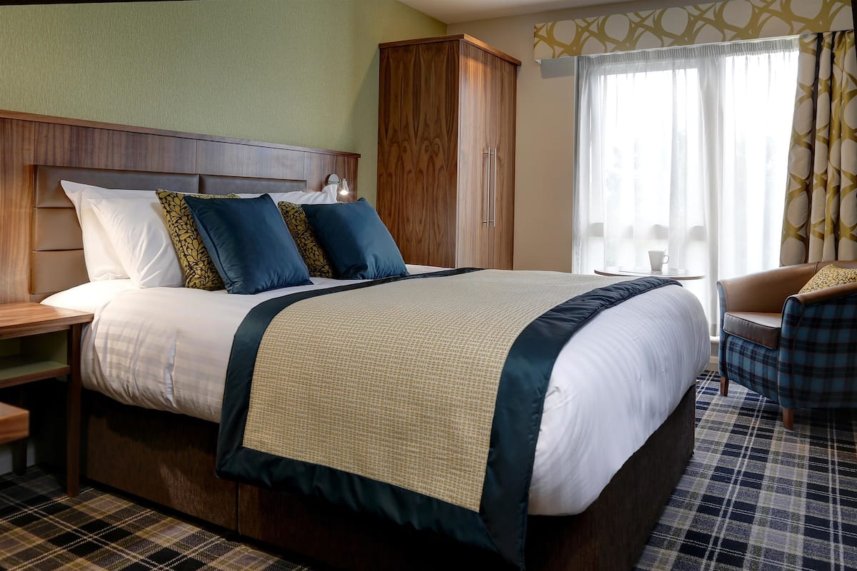 Ein Hotelzimmer mit einem großen Bett, einem Holzschrank, einem Stuhl und einem Fenster mit Vorhängen.