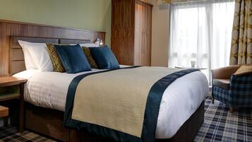 A hotel room with a large bed, a wooden wardrobe, a chair, and a window with curtains.