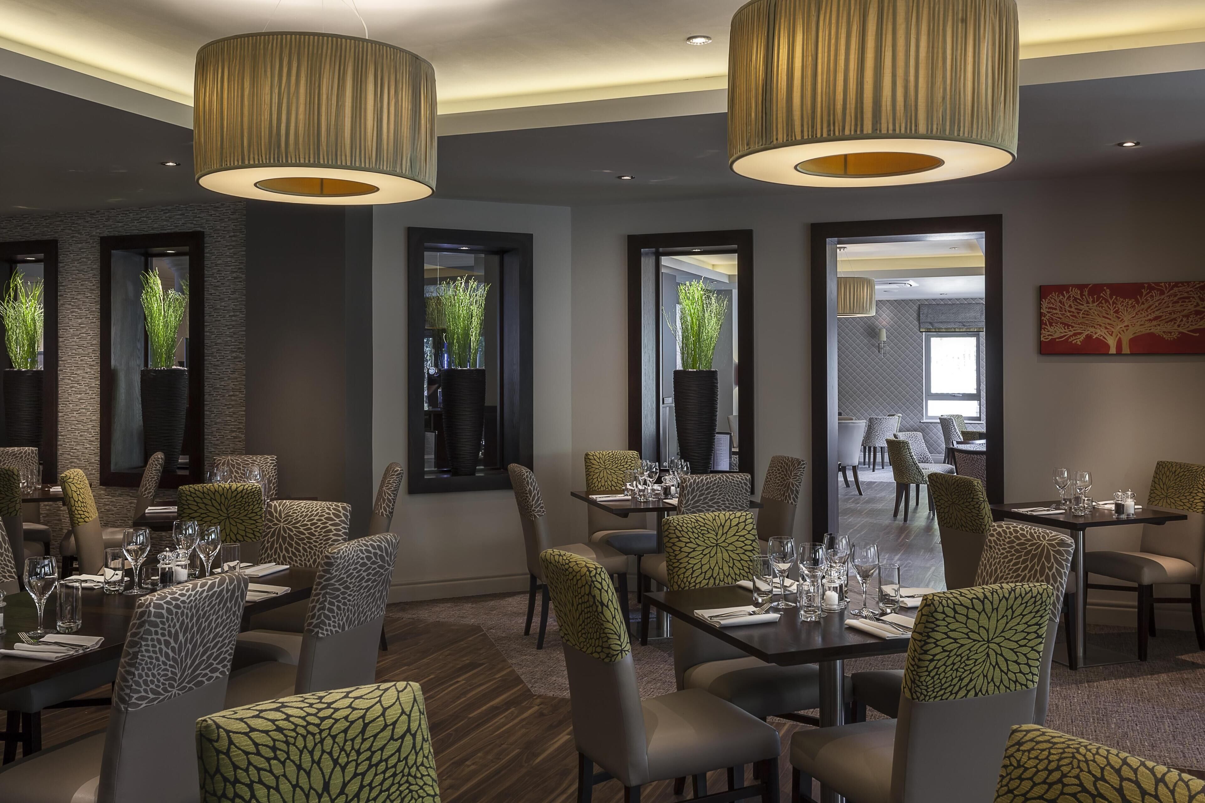 A restaurant with tables set for dining, large hanging lamps, and potted plants.