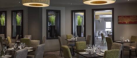 A restaurant with tables set for dining, large hanging lamps, and potted plants.