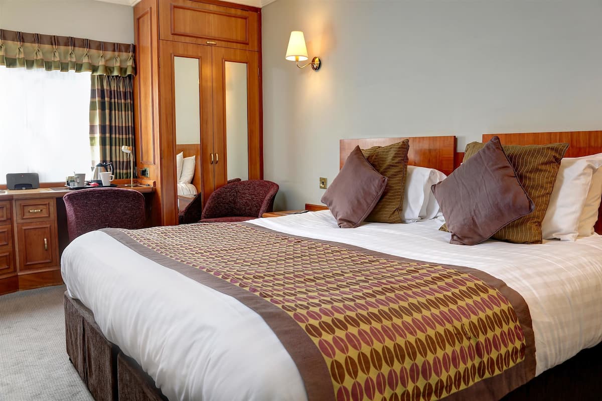 Ein Hotelzimmer mit einem großen Bett, einem Schreibtisch mit Stuhl, einem Kleiderschrank und einer Wandlampe.
