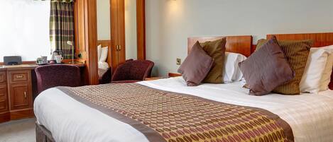 Quarto de hotel com uma cama grande, uma escrivaninha com cadeira, um guarda-roupa e uma luminária na parede.