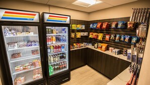 Una zona de autoservicio con aperitivos y bebidas, que incluye estantes refrigerados y una pared llena de bolsas de snack.