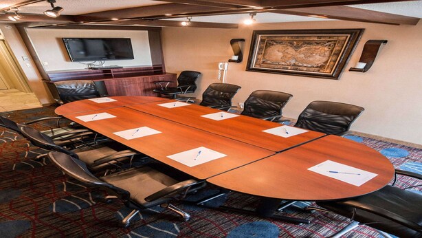 A conference room with a large oval table, black leather chairs, a flat-screen TV mounted on the wall, and a framed artwork above the table. - Wyndham Chicago O'Hare (Des Plaines)