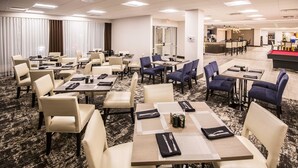 Un vestíbulo de hotel con varias zonas de estar, incluyendo mesas y sillas, y una mesa de billar.