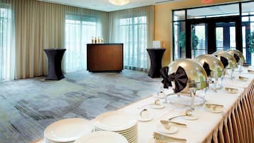 A banquet hall with a long table set for a formal event, featuring stacked plates and elegant tableware.