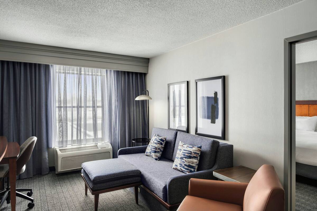 A hotel room with a sofa, a small table, a chair, a desk, and a bed.