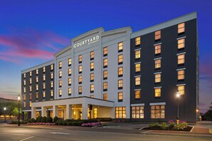 Un hotel de varios pisos con un letrero destacado de 'Courtyard by Marriott', una entrada central con zona techada y un estacionamiento con jardines.