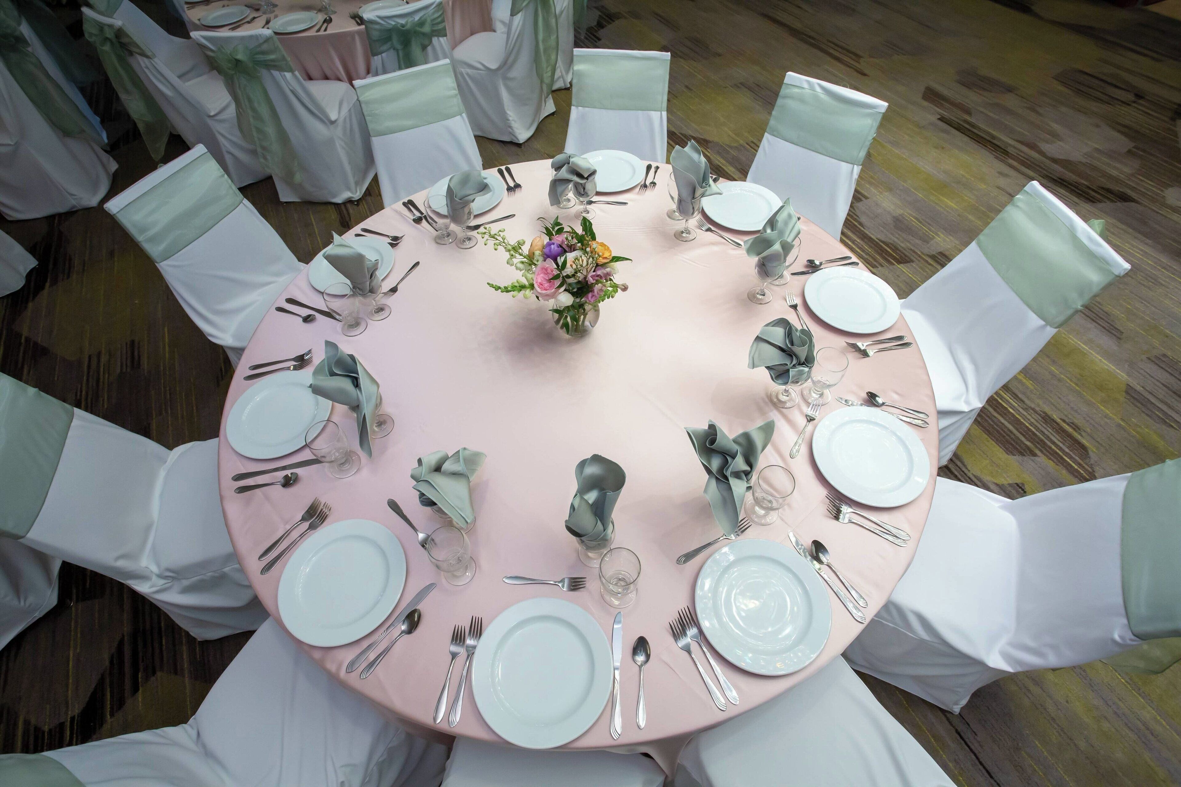 A round table with white chairs, each with a green sash, set for a formal event.