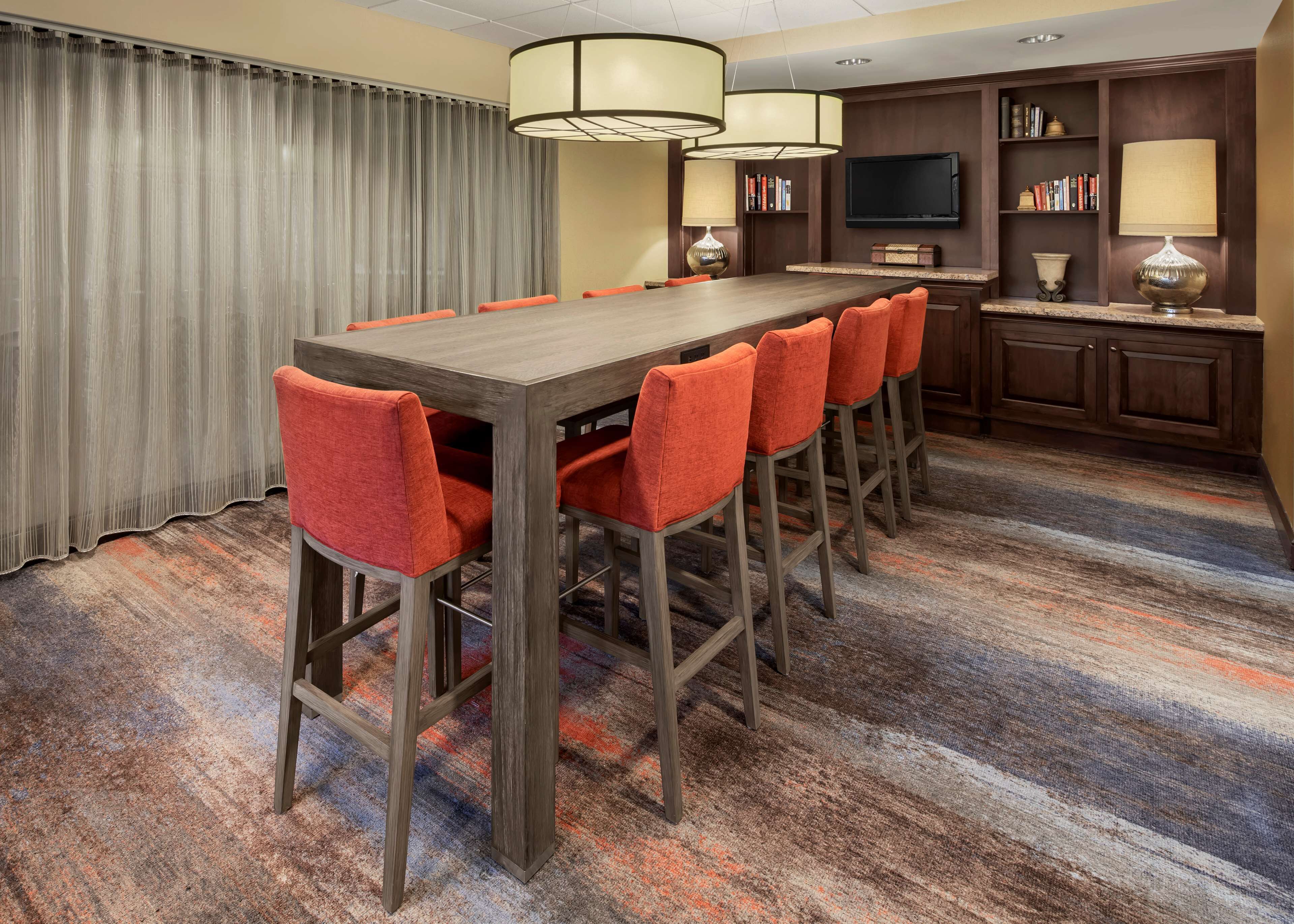 A hotel conference room with a long table, six orange chairs, a television, bookshelves, and lamps.