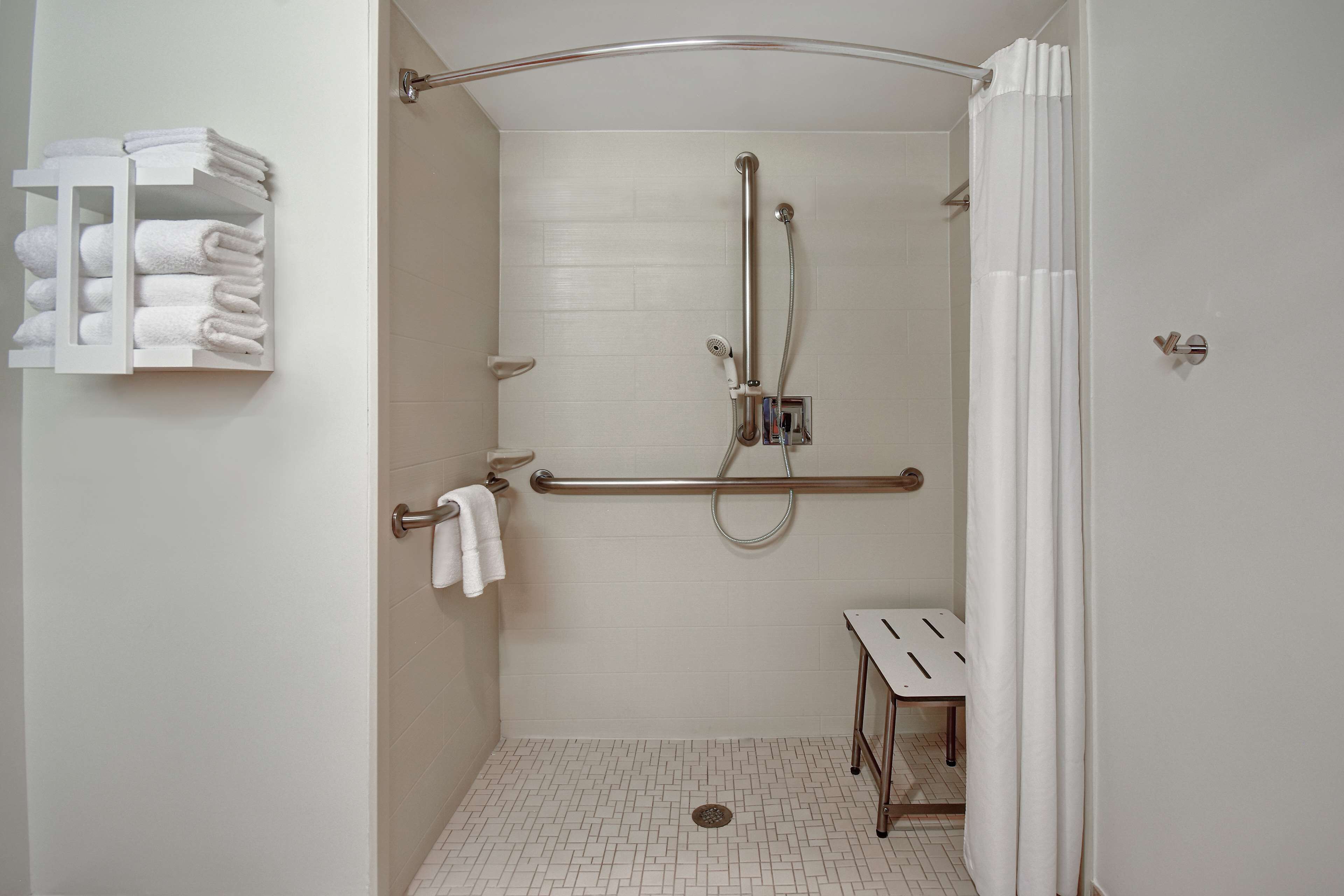 A walk-in shower with a grab bar, a white towel rack, and a small table.