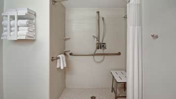 A walk-in shower with a grab bar, a white towel rack, and a small table.