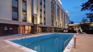 A swimming pool adjacent to a hotel with a modern design, a covered area with seating, and a clear sky. - Hampton Inn & Suites Alexandria Old Town Area South (Alexandria)