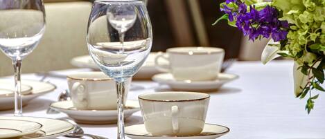 A table set with white plates, cups, and a wine glass, with a vase of flowers on the right.
