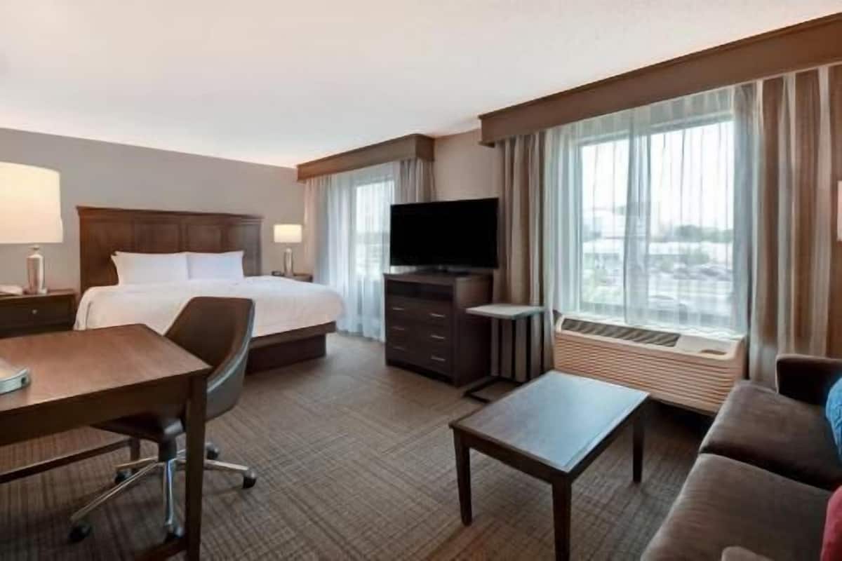 A hotel room with a bed, a desk, a television, a sofa, and a window with curtains.