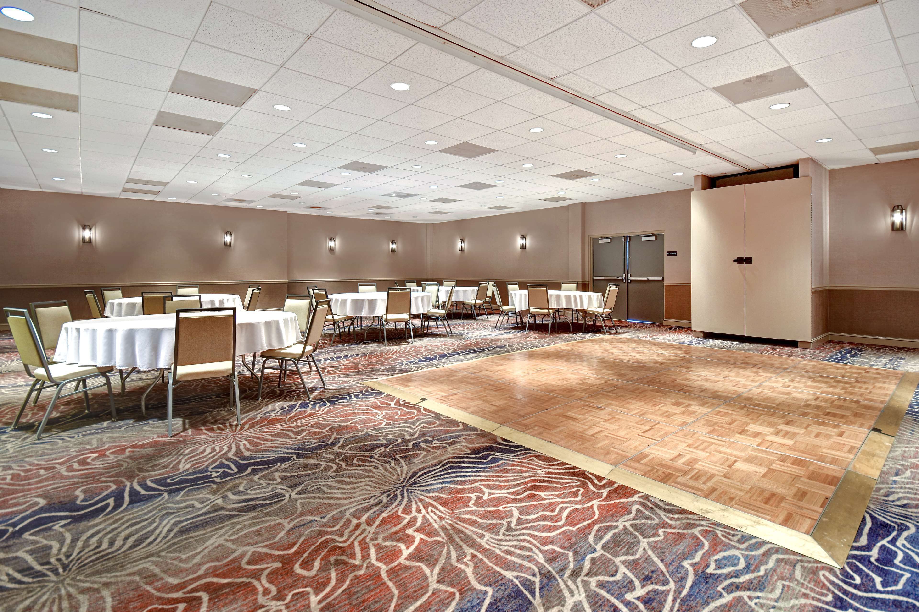A large conference room with multiple tables and chairs, a patterned carpet, and a plain ceiling with recessed lighting.