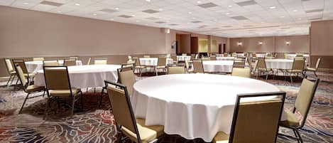 A conference room with round tables and chairs, carpeted flooring, and recessed lighting.