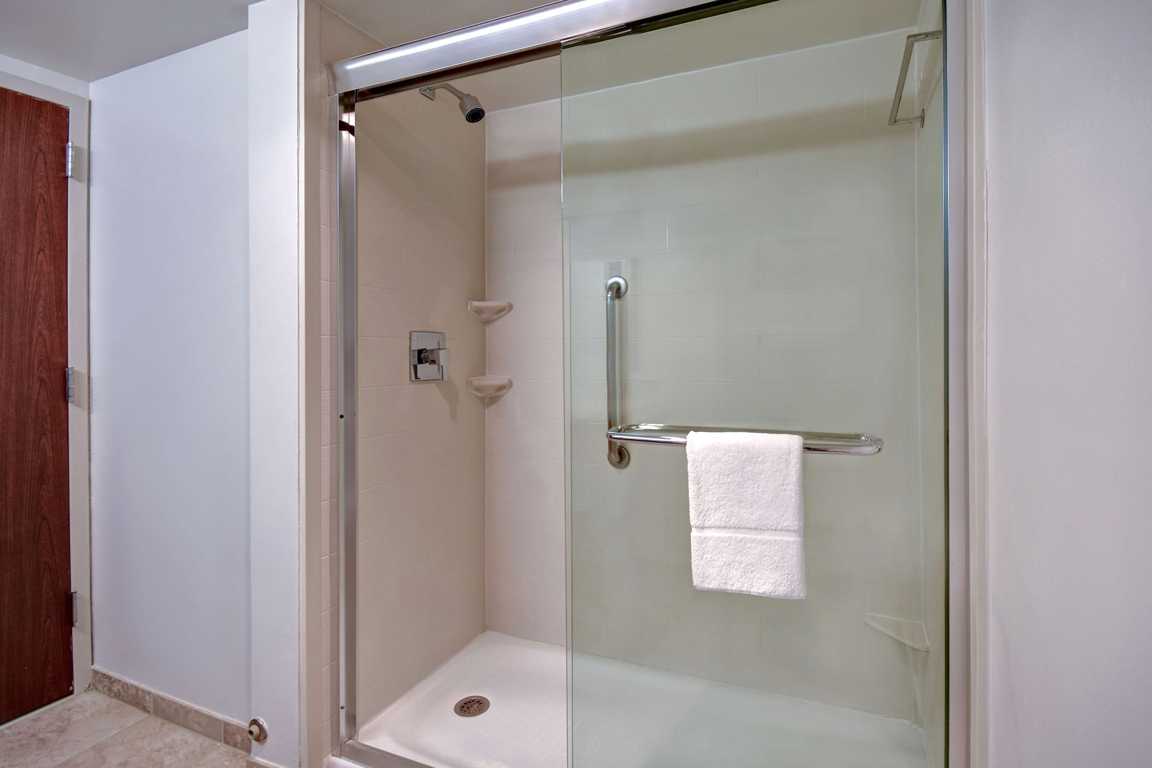 A glass-enclosed shower stall with a white towel hanging on a metal bar.