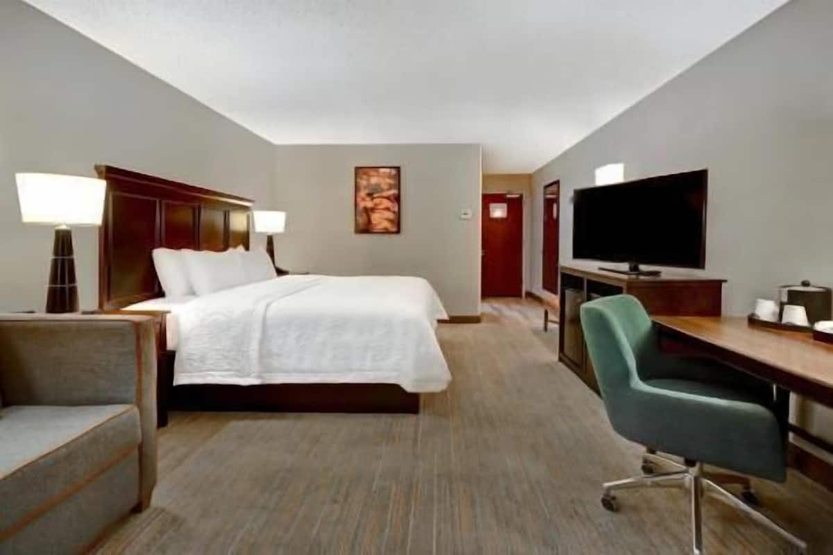 A hotel room with a bed, desk, chair, TV, and a painting on the wall.