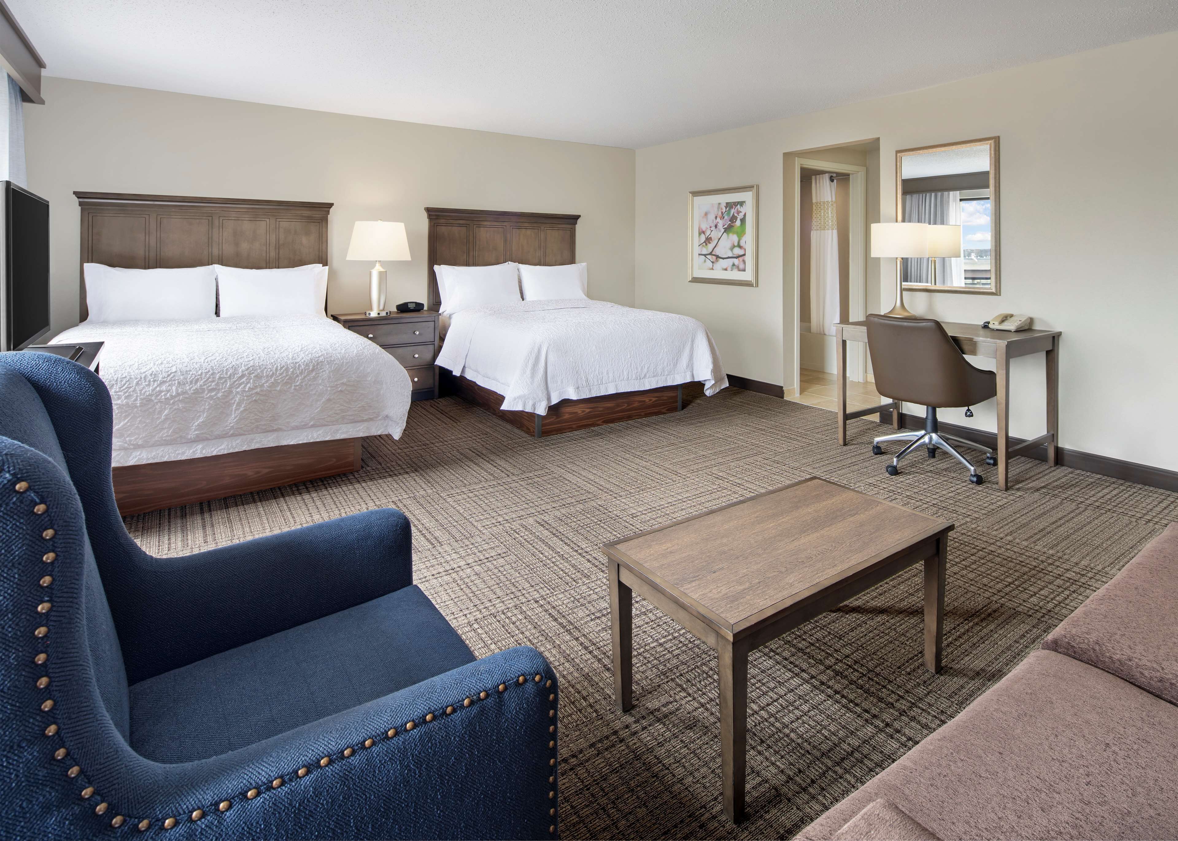 A hotel room with two beds, a desk, a chair, and a small table.