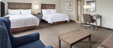 A hotel room with two beds, a desk, a chair, and a small table.