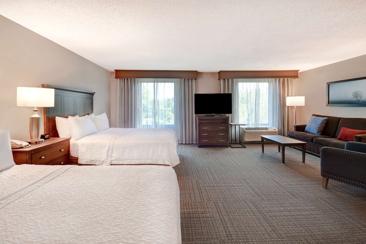 A hotel room with two beds, a sofa, a TV, and a desk.