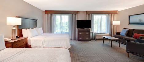A hotel room with two beds, a sofa, a TV, and a desk.