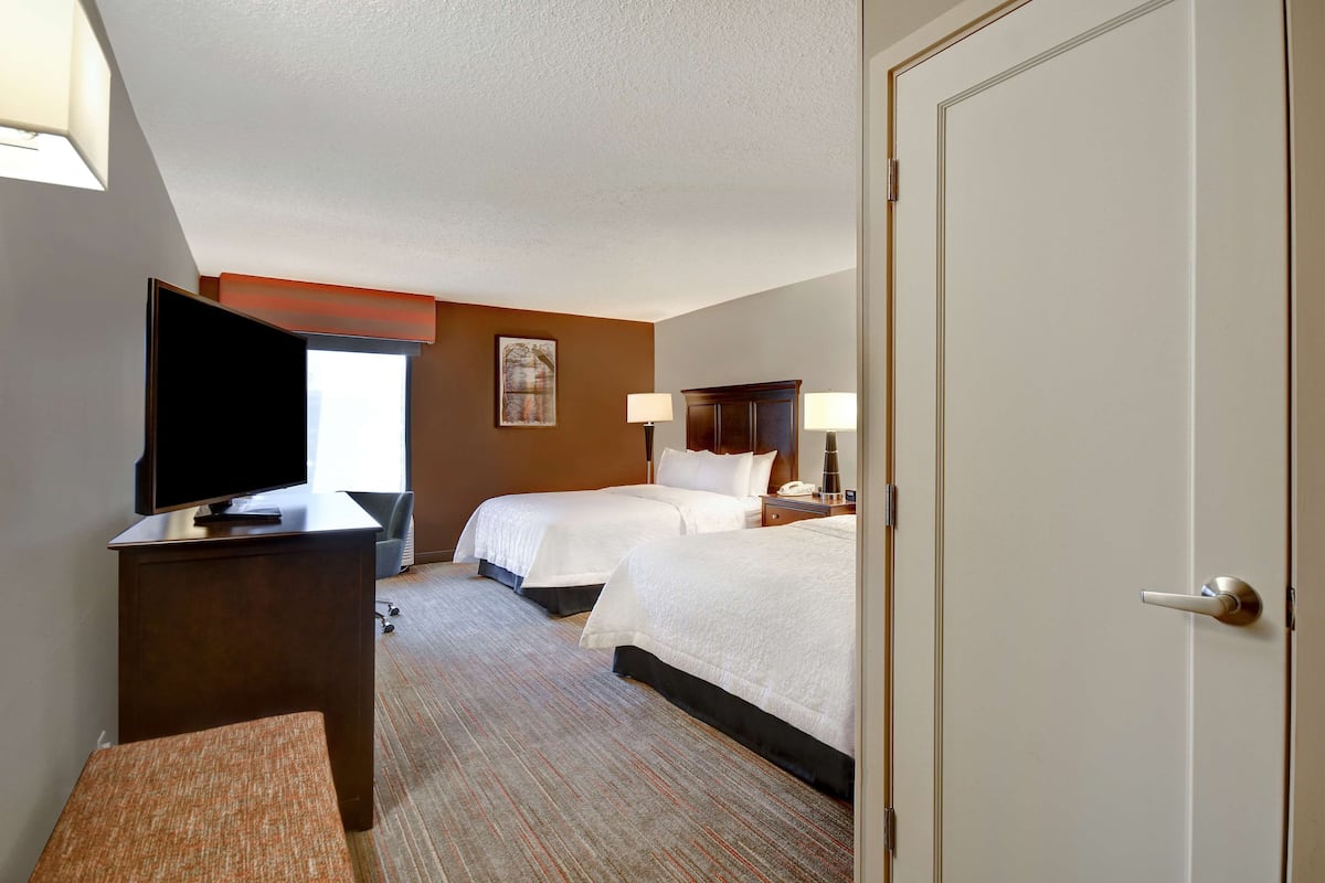 A hotel room with two beds, a desk with a TV, and a door.