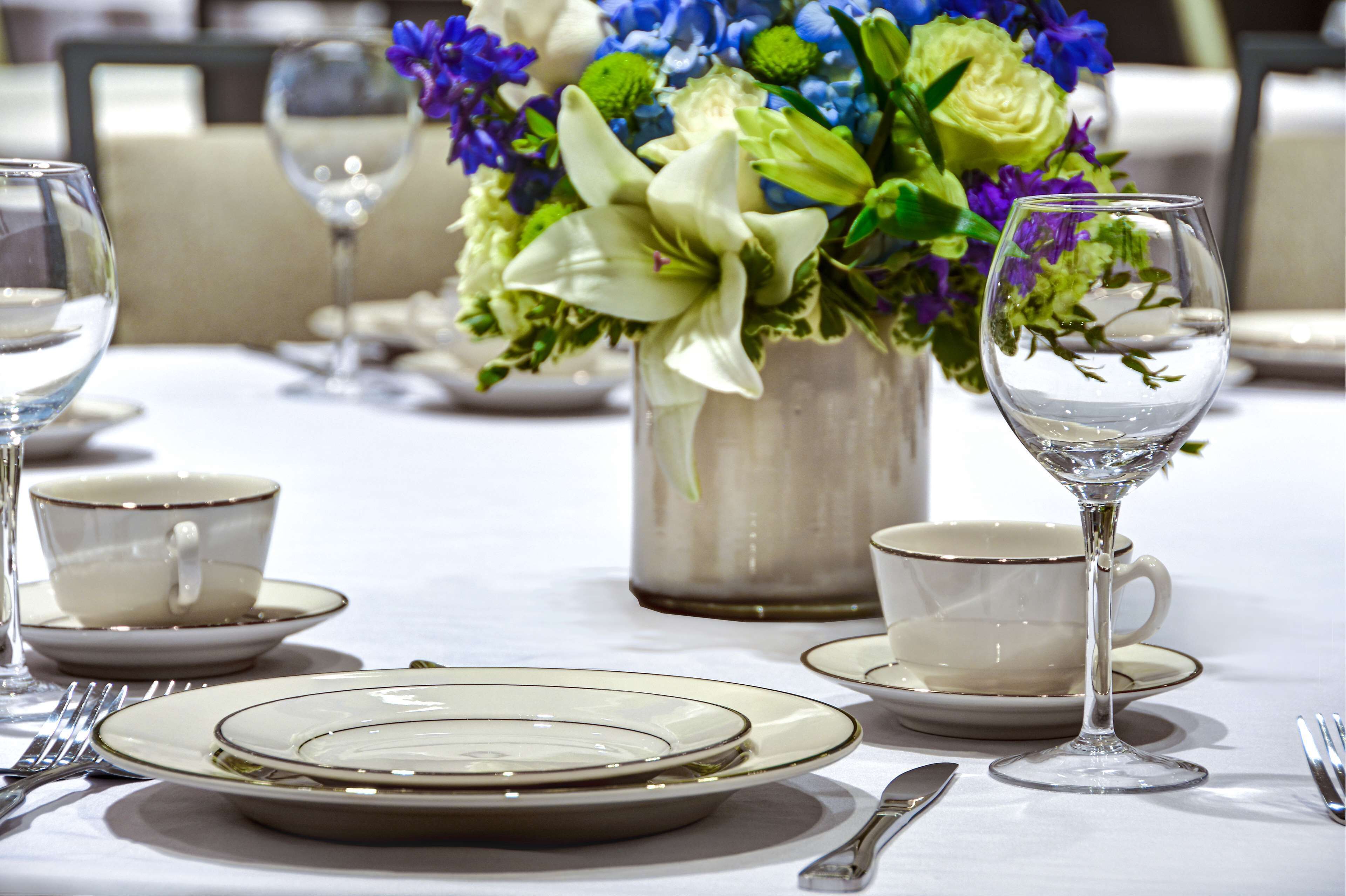 A table set with plates, cups, and cutlery, with a vase of flowers in the background.
