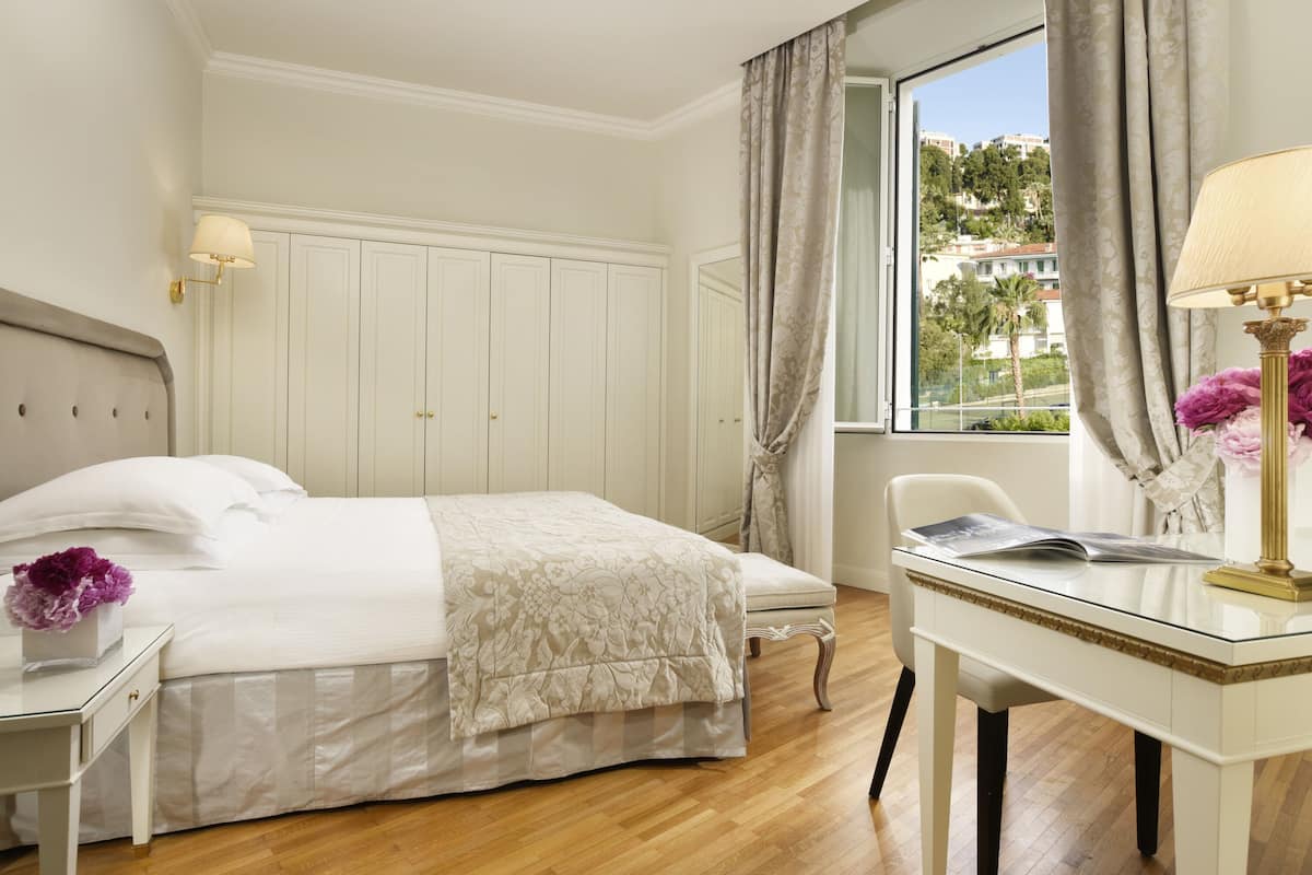 A hotel room with a bed, a desk, and a window with curtains.