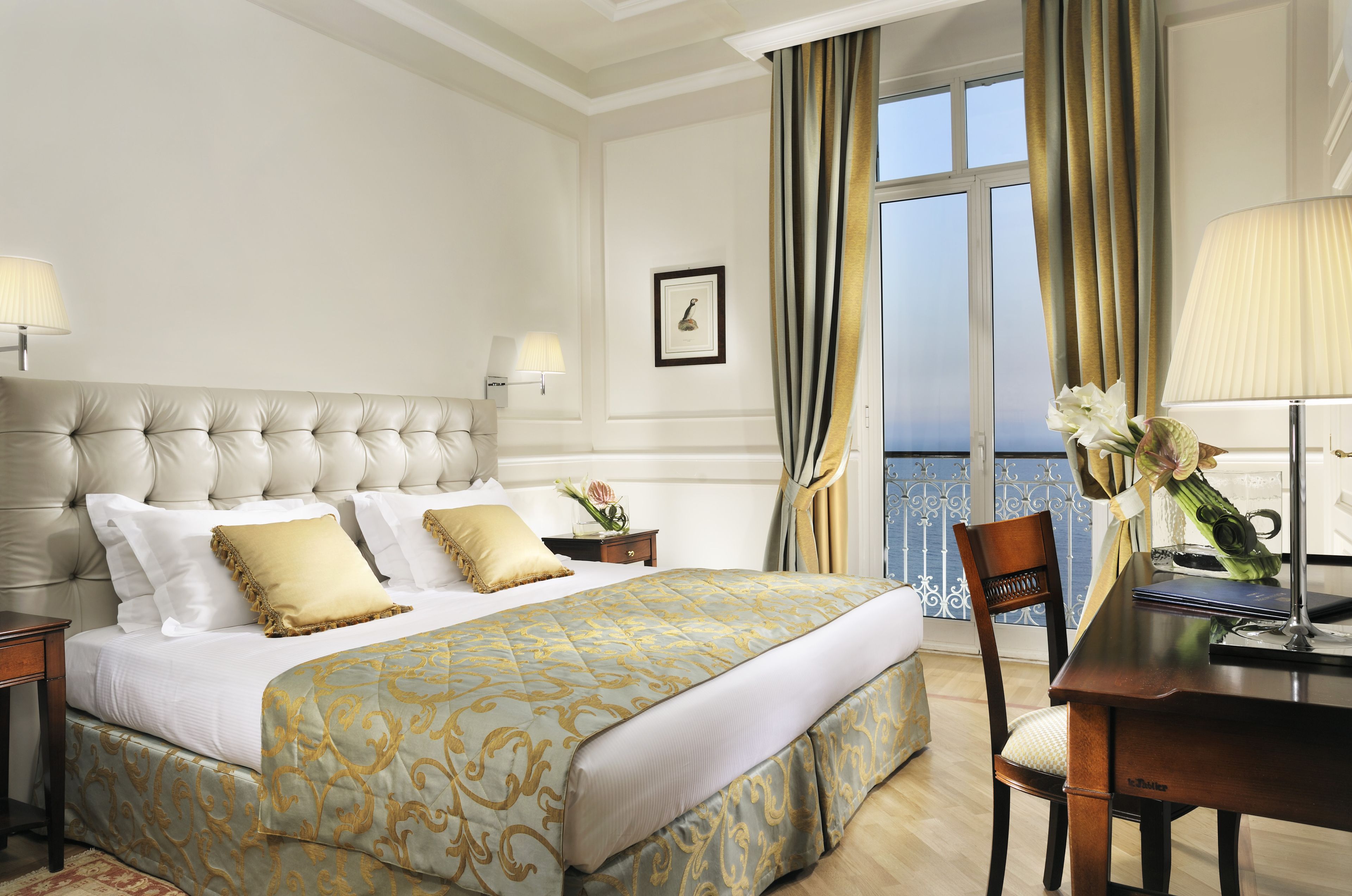 A hotel room with a large bed, a desk, and a view of the sea.