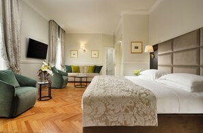 A hotel room with a bed, a sofa, a coffee table, and a TV on the wall.