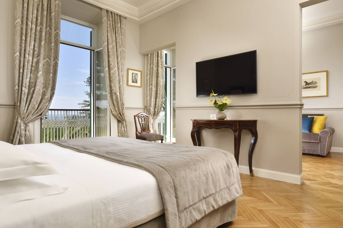 A hotel room with a large bed, a television mounted on the wall, and a view of the outside balcony.