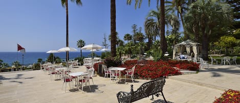 Un espacio al aire libre con mesas y sillas, un pabellón y vistas al mar.