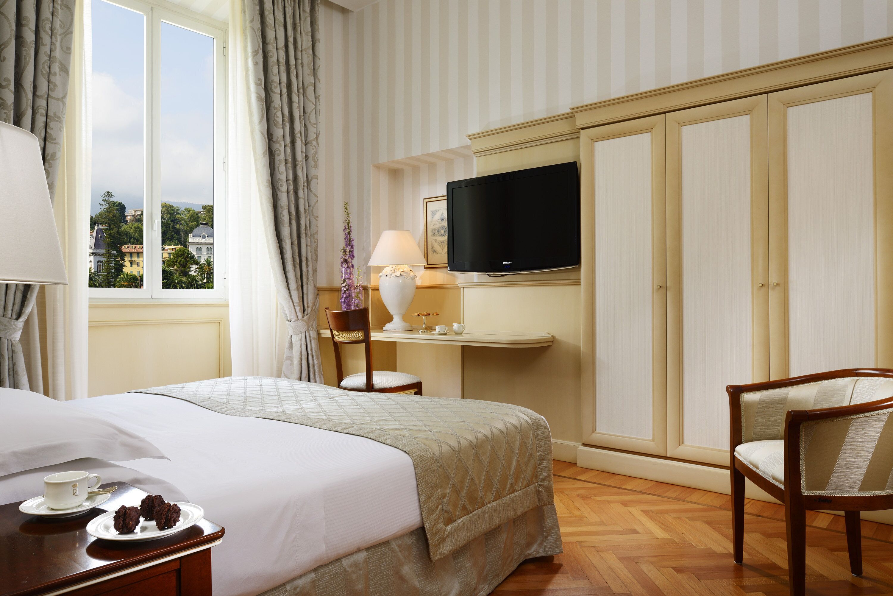 Una habitación de hotel con cama, televisión, escritorio con lámpara y una silla.