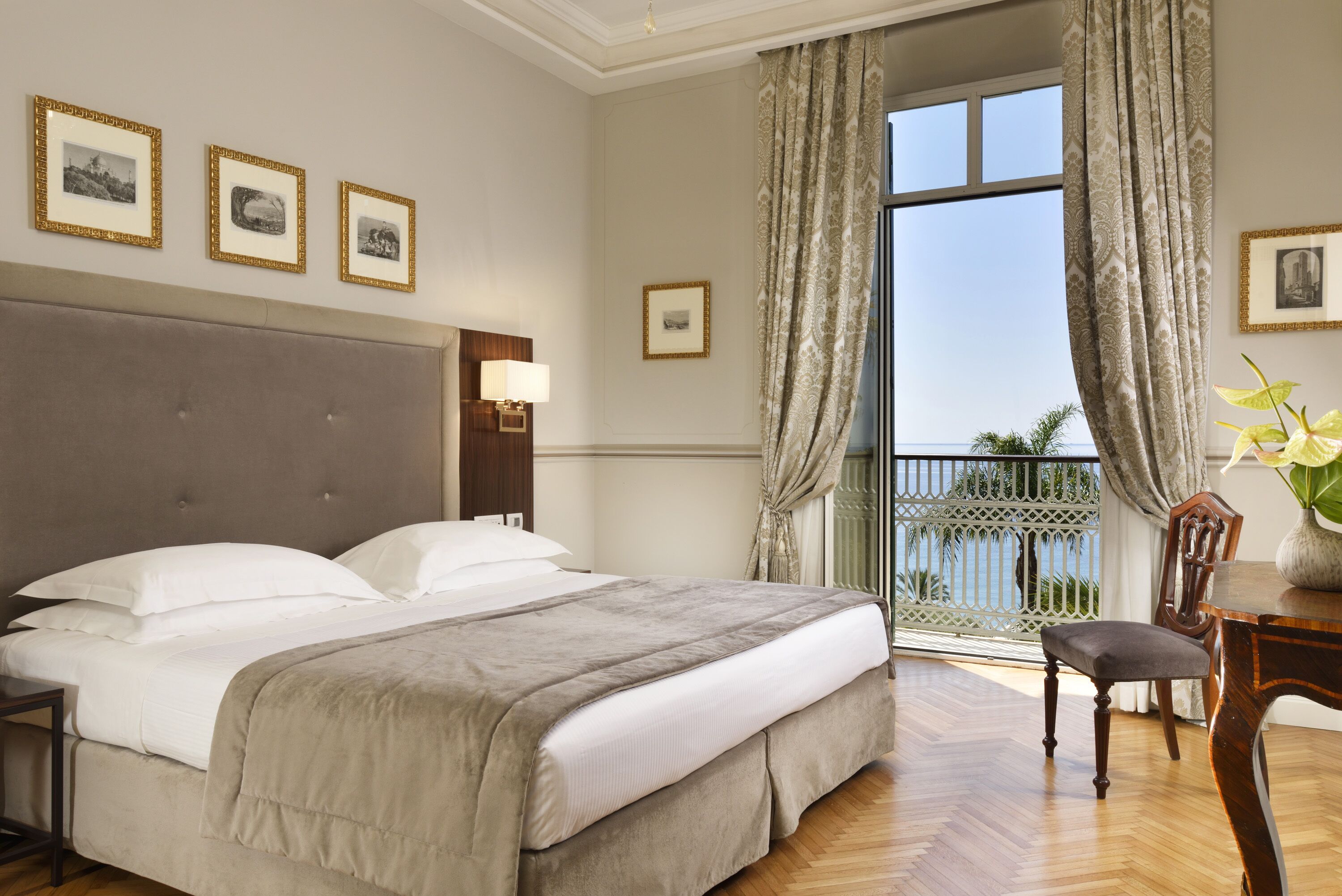 Habitación de hotel con una cama grande, una silla de madera, un escritorio y un balcón con vistas.
