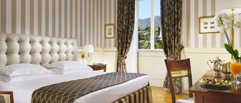 Habitación de hotel con una cama grande, una mesa de comedor y una jarra de zumo de naranja, y vistas a la montaña a través de la ventana.