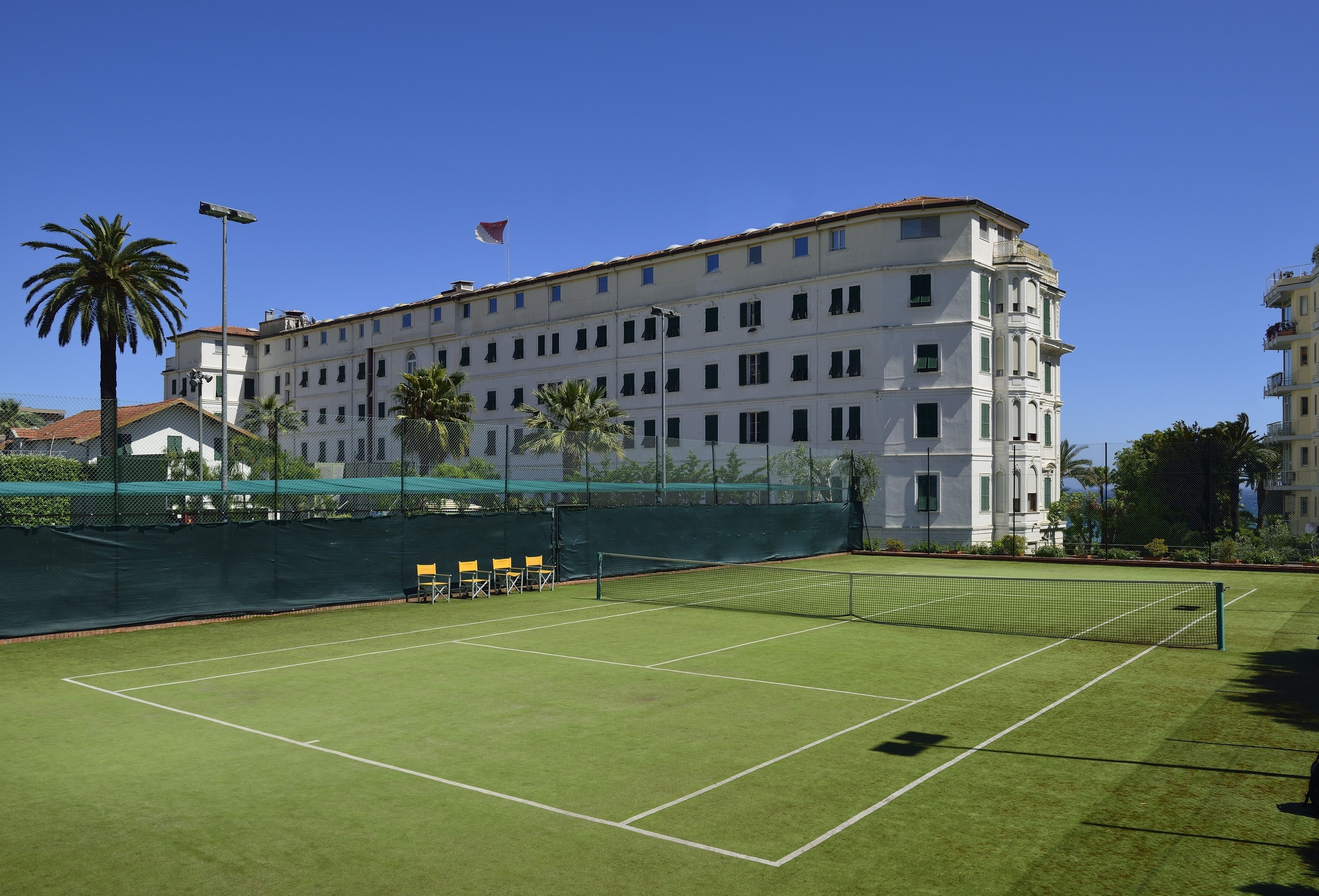 Un court de tennis avec un filet, entouré d’une clôture et de palmiers.