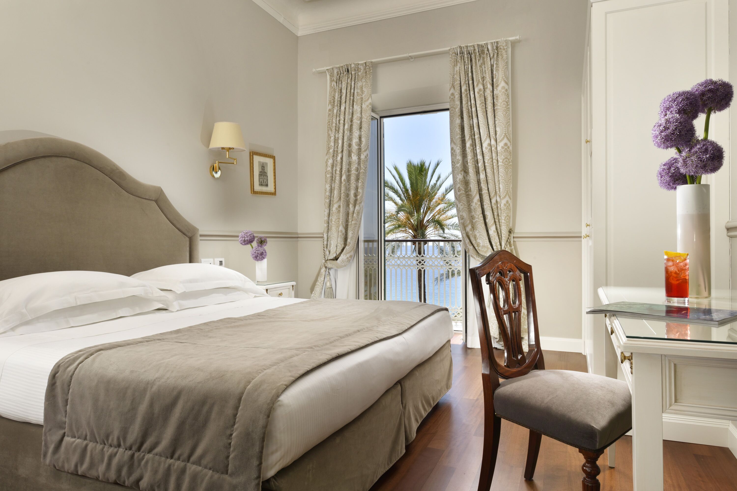 A hotel room with a bed, a chair, a desk with a glass top, and a view of the outside.