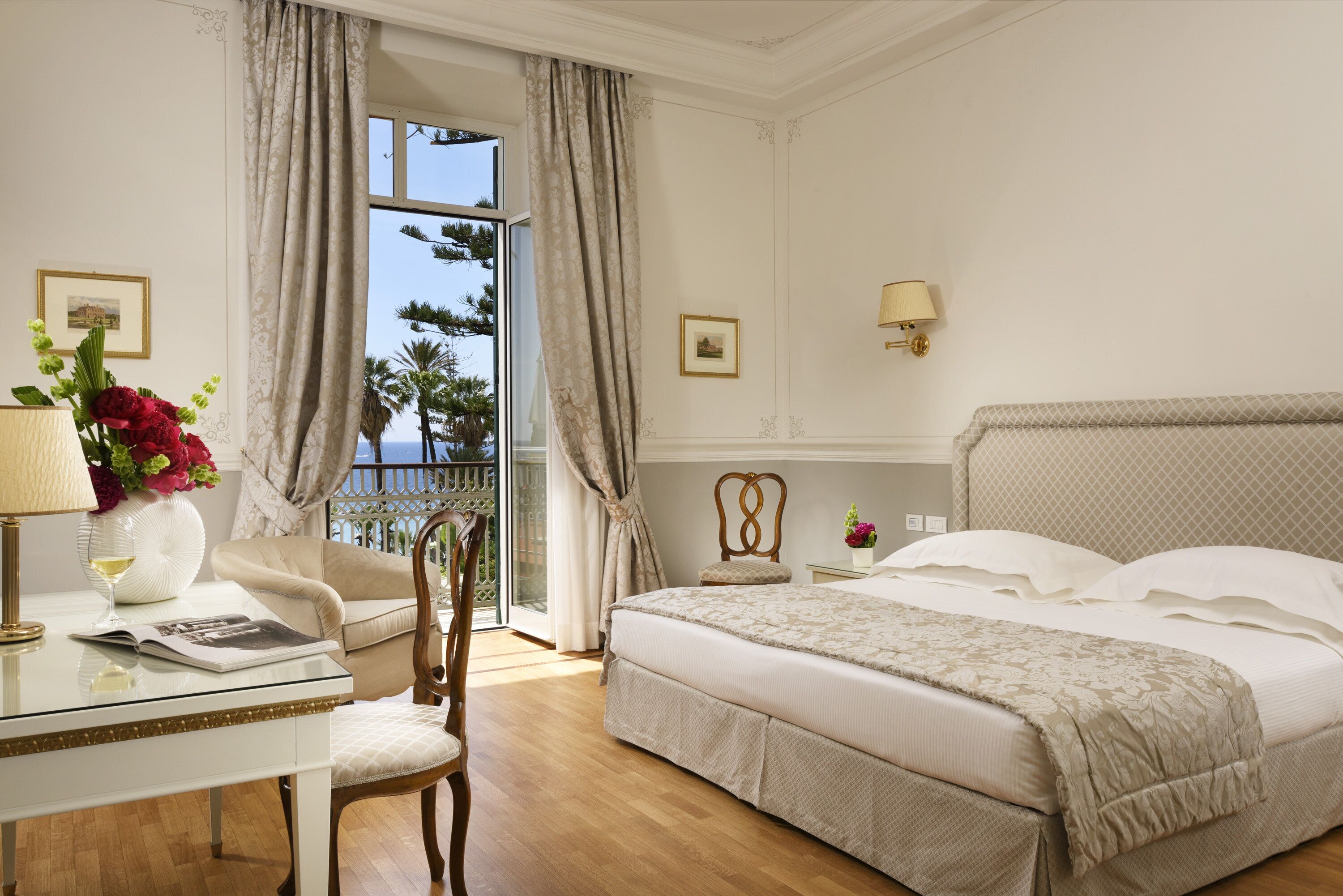 A hotel room with a bed, a desk with a lamp, a chair, and a view of the outdoors.
