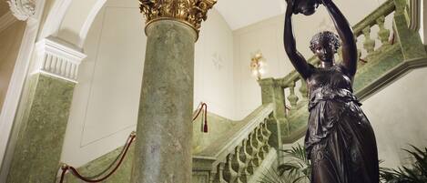 A grand staircase with a statue, marble columns, and ornate architectural details.