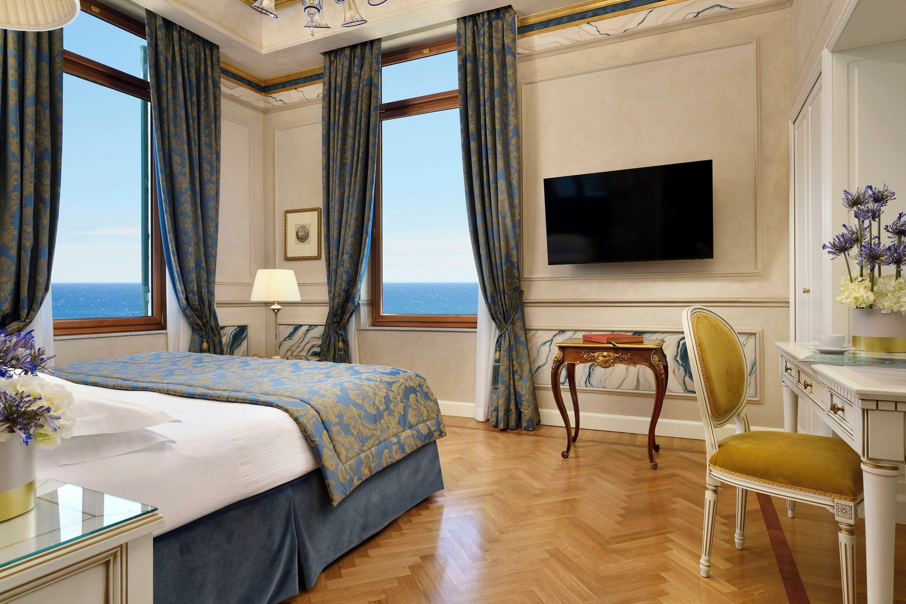 Habitación de hotel con una cama grande, televisión, escritorio con silla y vista al mar.