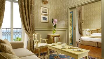 Habitación de hotel con balcón, cama, zona de estar con sofá y sillón, una mesita con juego de té y un florero con flores.