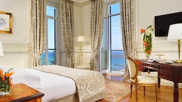 A hotel room with a bed, a desk, a chair, a TV, and a balcony with curtains.