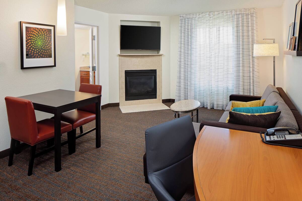 Habitación de hotel con una mesa de comedor, sillas, un sofá, chimenea, televisión y lámpara.