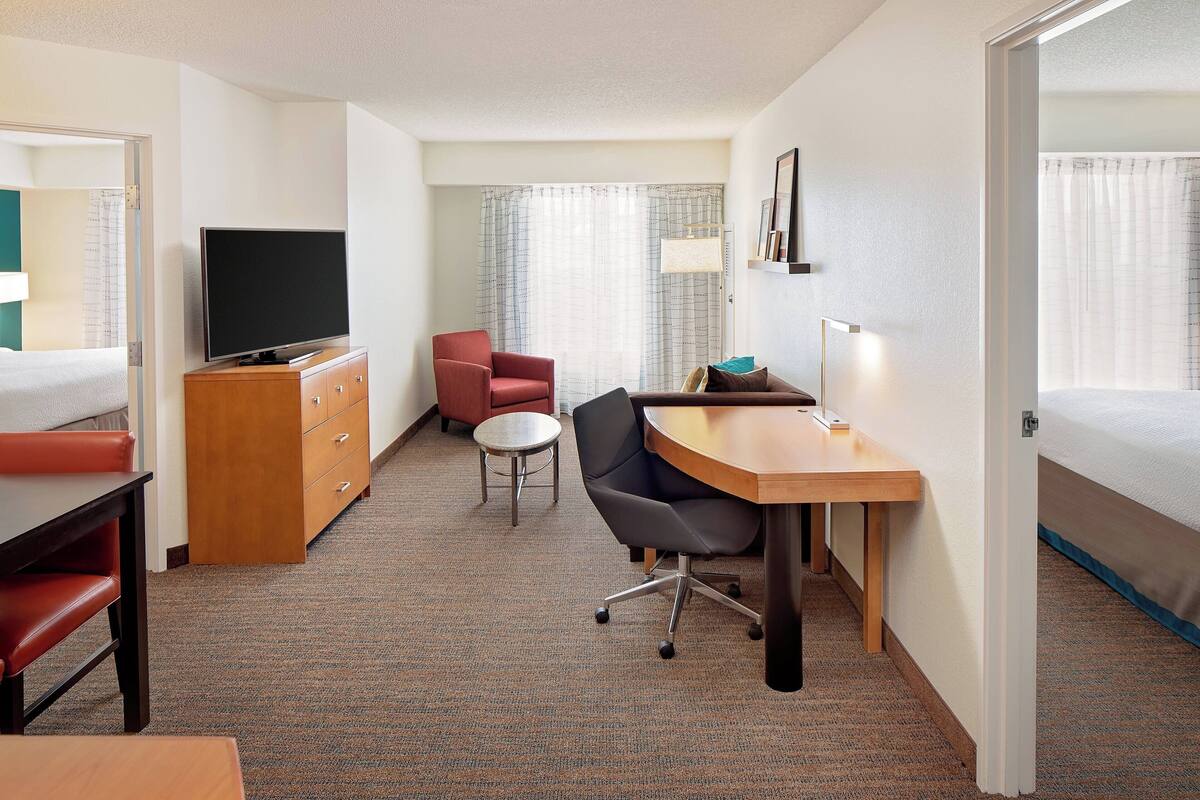 Habitación de hotel con cama, escritorio con silla, televisión, mesita y armario.